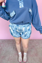 Load image into Gallery viewer, Person wearing a blue outfit with floral patterns against a pink background