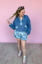Load image into Gallery viewer, Woman wearing a blue outfit with floral shorts against a pink background