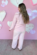 Load image into Gallery viewer, Woman in a pink outfit standing against a pink wall with heart decorations
