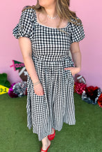 Load image into Gallery viewer, Girl wearing a black and white gingham midi dress with red jelly flats in front of a pink game day backdrop.