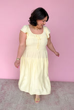 Load image into Gallery viewer, Woman wearing a light yellow midi dress against a pink background