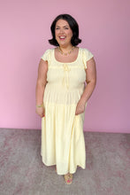 Load image into Gallery viewer, Woman wearing a light yellow midi dress against a pink background