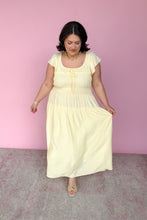 Load image into Gallery viewer, Woman wearing a light yellow midi dress against a pink background
