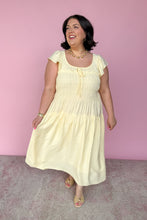 Load image into Gallery viewer, Woman wearing a light yellow midi dress against a pink background