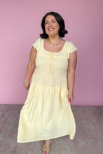 Load image into Gallery viewer, Woman wearing a light yellow midi dress against a pink background