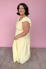 Load image into Gallery viewer, Woman wearing a light yellow midi dress against a pink wall side view