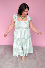 Load image into Gallery viewer, Woman wearing a green and white floral striped midi dress against a pink background
