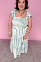 Load image into Gallery viewer, Woman wearing a green and white floral striped midi dress against a pink background