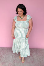Load image into Gallery viewer, Woman wearing a green and white floral striped midi dress against a pink background