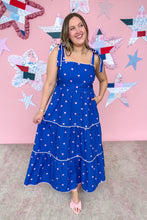 Load image into Gallery viewer, Woman in a blue polka dot dress standing in front of a pink wall with star decorations.