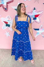 Load image into Gallery viewer, Woman in a blue polka dot dress standing in front of a pink wall with star-shaped decorations.