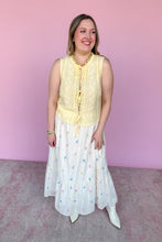 Load image into Gallery viewer, Woman wearing a yellow sleeveless top and white skirt with colorful embroidered flowers against a pink background