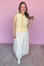 Load image into Gallery viewer, Woman wearing a yellow sleeveless top and white skirt with colorful embroidered flowers against a pink background