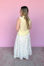 Load image into Gallery viewer, Woman wearing a yellow sleeveless top and white skirt with colorful embroidered flowers against a pink background back view