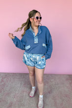 Load image into Gallery viewer, Woman wearing a blue outfit with floral patterns against a pink wall.