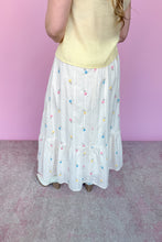 Load image into Gallery viewer, Woman wearing a yellow sleeveless top and white skirt with colorful embroidered floral pattern against a pink background Back view