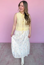 Load image into Gallery viewer, Woman wearing a yellow sleeveless top and white skirt with colorful embroidered floral pattern against a pink background