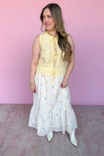 Load image into Gallery viewer, Woman wearing a yellow sleeveless top and white skirt with colorful embroidered floral pattern against a pink background