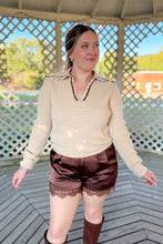 Load image into Gallery viewer, Girl wearing a cream collared sweater, brown lace satin shorts, and brown knee high boots while standing in a gazebo.