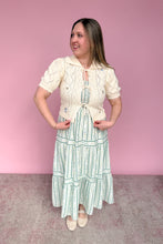 Load image into Gallery viewer, Woman wearing a vintage-style outfit with a white blouse and green striped skirt against a pink background
