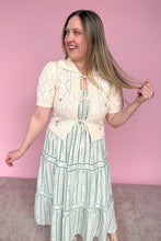 Load image into Gallery viewer, Woman wearing a cream cardigan over a striped dress against a pink background