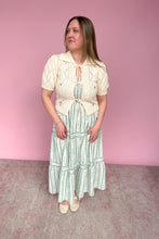 Load image into Gallery viewer, Woman wearing a cream blouse and green striped skirt against a pink background