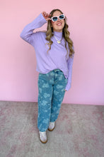 Load image into Gallery viewer, Woman wearing a light purple turtleneck and denim floral pants against a pink background
