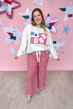 Load image into Gallery viewer, Woman wearing a white sweatshirt with a red and blue graphic and red checkered pants against a pink wall with star decorations.