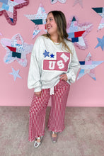 Load image into Gallery viewer, Woman wearing a white sweatshirt with a red and blue design and red checkered pants in front of a pink wall with star decorations.