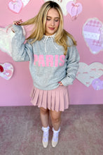 Load image into Gallery viewer, Person wearing a gray sweatshirt with 'PARIS' in pink and a pink skirt against a pink heart-themed background.