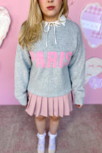 Load image into Gallery viewer, Person wearing a gray sweatshirt with pink text and a pink pleated skirt against a pink background.