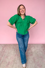 Load image into Gallery viewer, Woman wearing a green blouse and blue jeans against a pink background