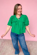 Load image into Gallery viewer, Woman wearing a green blouse and blue jeans against a pink background