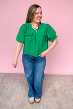 Load image into Gallery viewer, Woman wearing a green blouse and blue jeans against a pink background