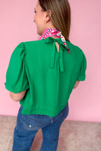 Load image into Gallery viewer, Woman wearing a green blouse and blue jeans standing against a pink background back view