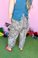 Load image into Gallery viewer, A person shown from the back wearing gray and white leopard print pants, a blue denim vest, and red shoes, standing on green artificial turf against a pink wall with colorful decorations.