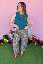 Load image into Gallery viewer, A woman modeling a sleeveless blue denim vest and gray-and-white leopard print pants with red shoes, standing on artificial green turf against a pink backdrop with decorative tinsel and signs.