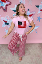 Load image into Gallery viewer, Woman wearing a pink shirt with an American flag design and red checkered pants, standing in front of a star-patterned wall.