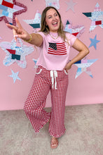 Load image into Gallery viewer, Woman in pink t-shirt with American flag design and red checkered pants posing in front of a star-patterned wall.