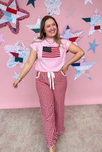 Load image into Gallery viewer, Woman wearing a pink t-shirt with an American flag design and red checkered pants, standing in front of a star-patterned wall.