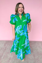 Load image into Gallery viewer, Woman wearing a green dress with blue floral pattern against a pink background