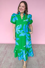 Load image into Gallery viewer, Woman wearing a green and blue floral dress against a pink background