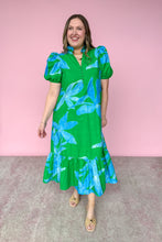 Load image into Gallery viewer, Woman wearing a green and blue floral dress against a pink background