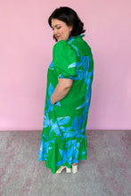 Load image into Gallery viewer, Woman wearing a green dress with blue floral pattern against a pink background