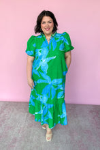 Load image into Gallery viewer, Woman wearing a green and blue floral dress against a pink background
