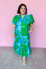 Load image into Gallery viewer, Woman wearing a green dress with blue floral pattern against a pink background