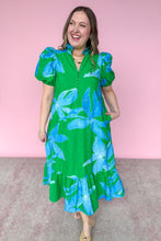 Load image into Gallery viewer, Woman wearing a green dress with blue floral pattern against a pink background
