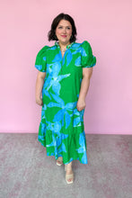 Load image into Gallery viewer, Woman wearing a green dress with blue floral patterns against a pink background