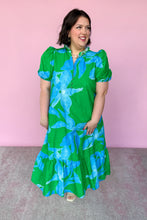 Load image into Gallery viewer, Woman wearing a green and blue floral dress against a pink background