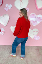 Load image into Gallery viewer, Person wearing a red sweater and blue jeans standing in front of a pink wall with heart decorations.